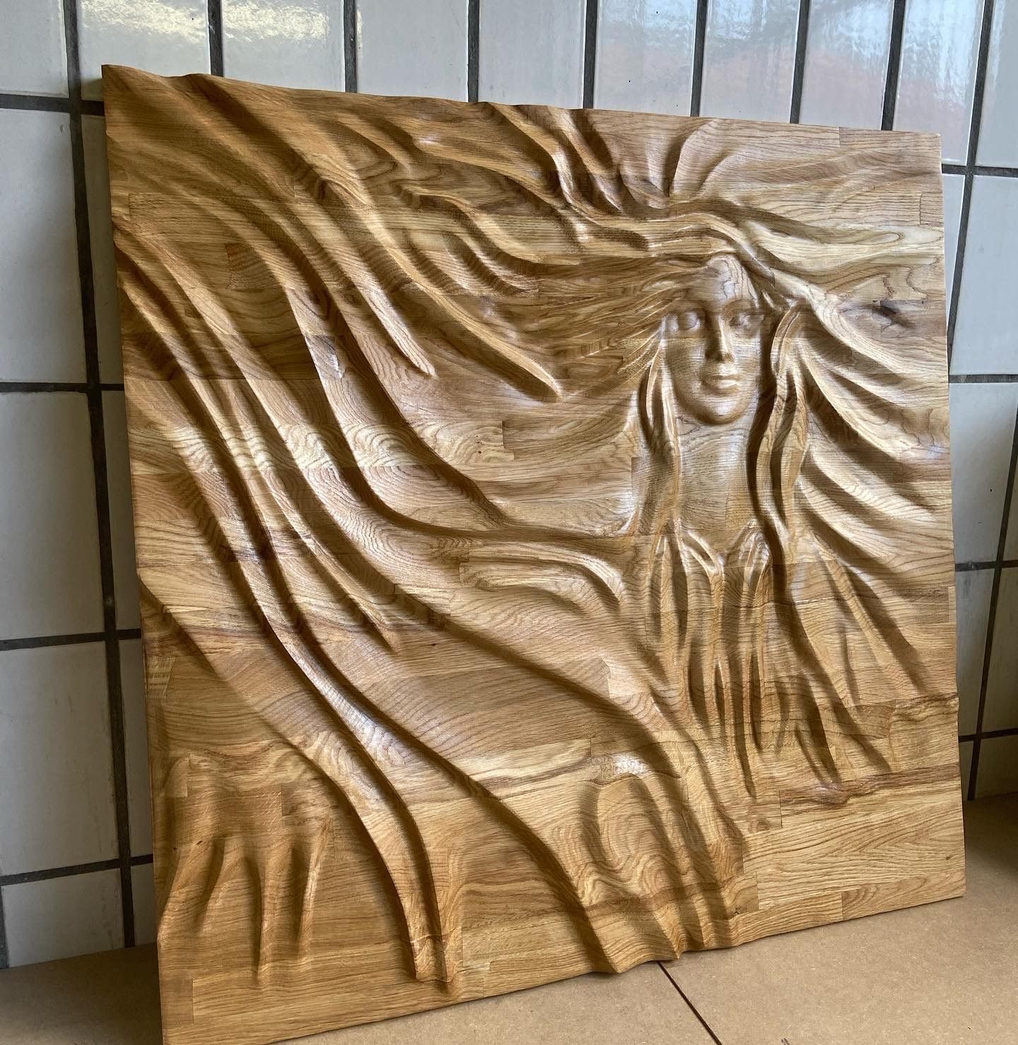 An art installation piece: a woman's face carved as a relief into a solid oak panel, around a metre square