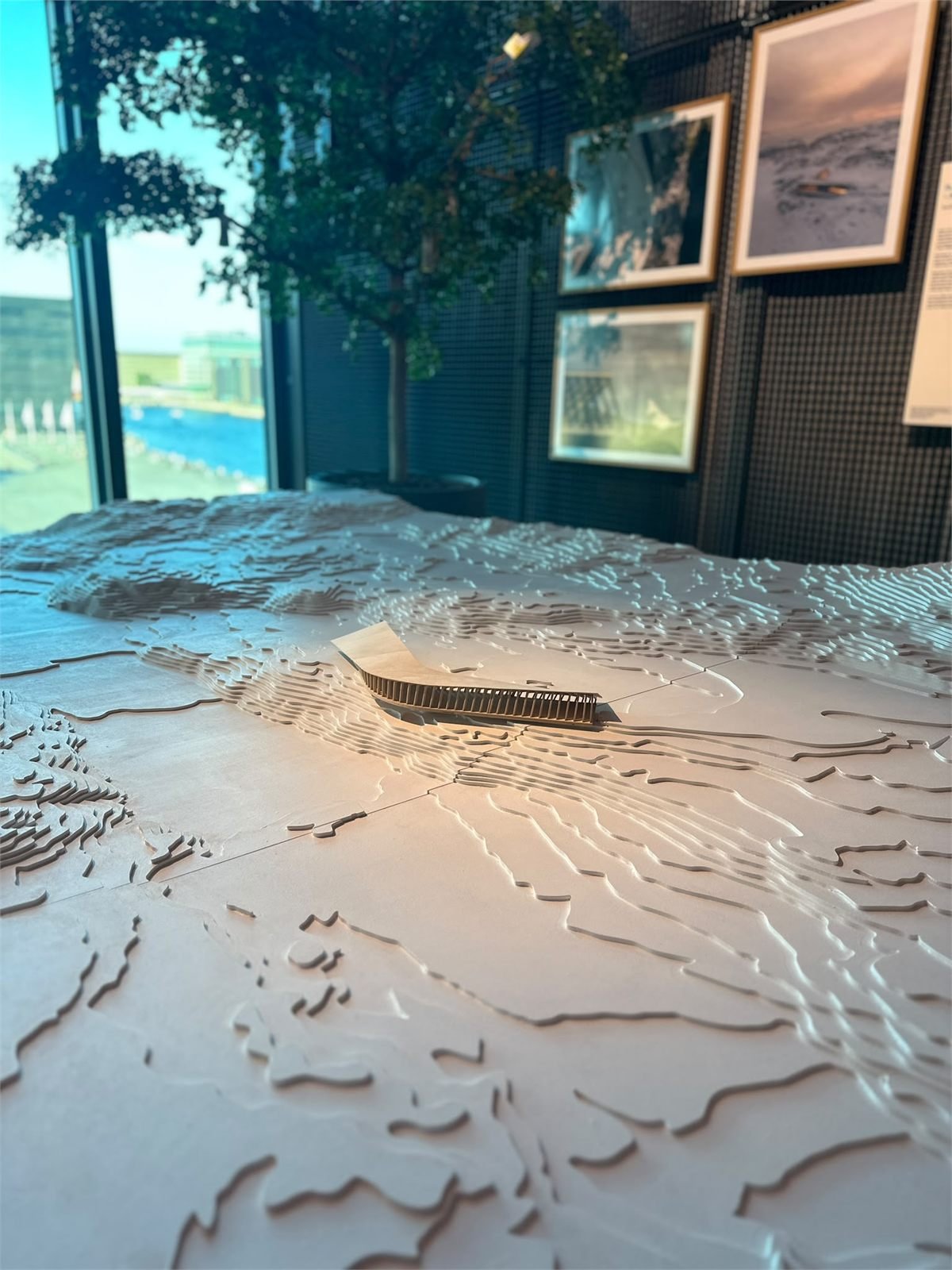 Contoured terrain model with a small building, shown in an architecture exhibition