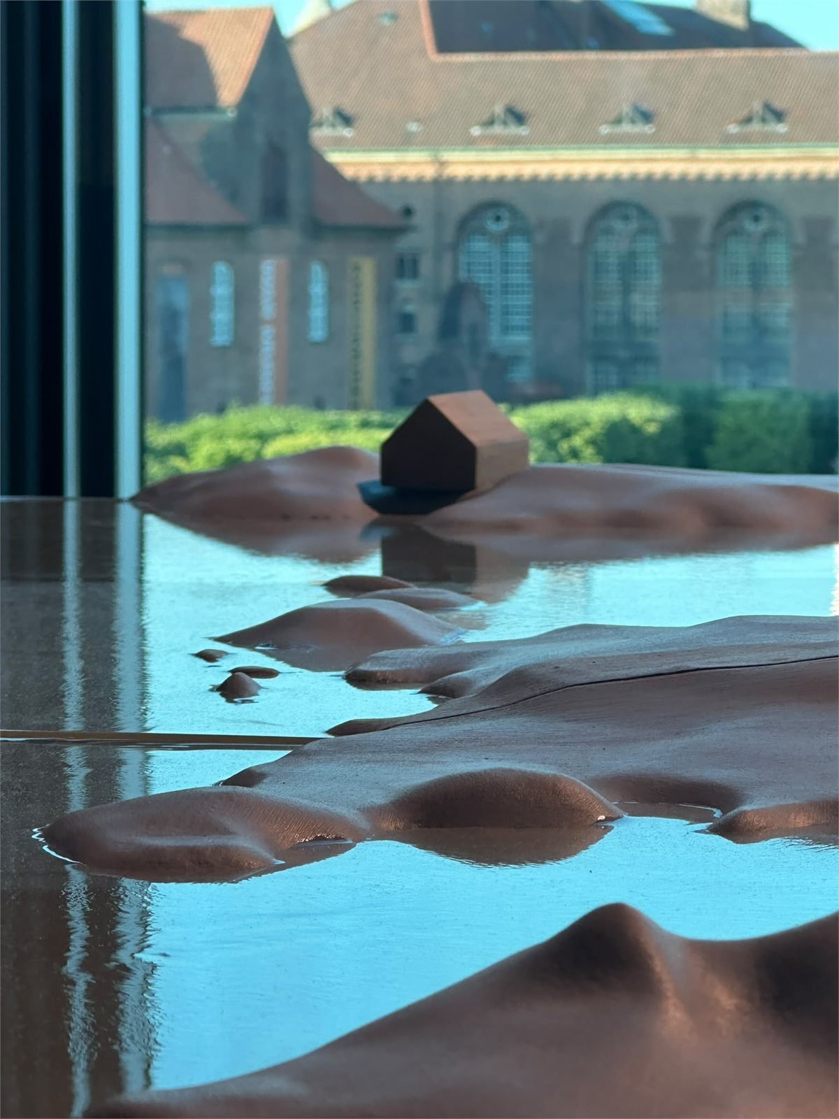 Terrain model with water and a small house, lit by daylight