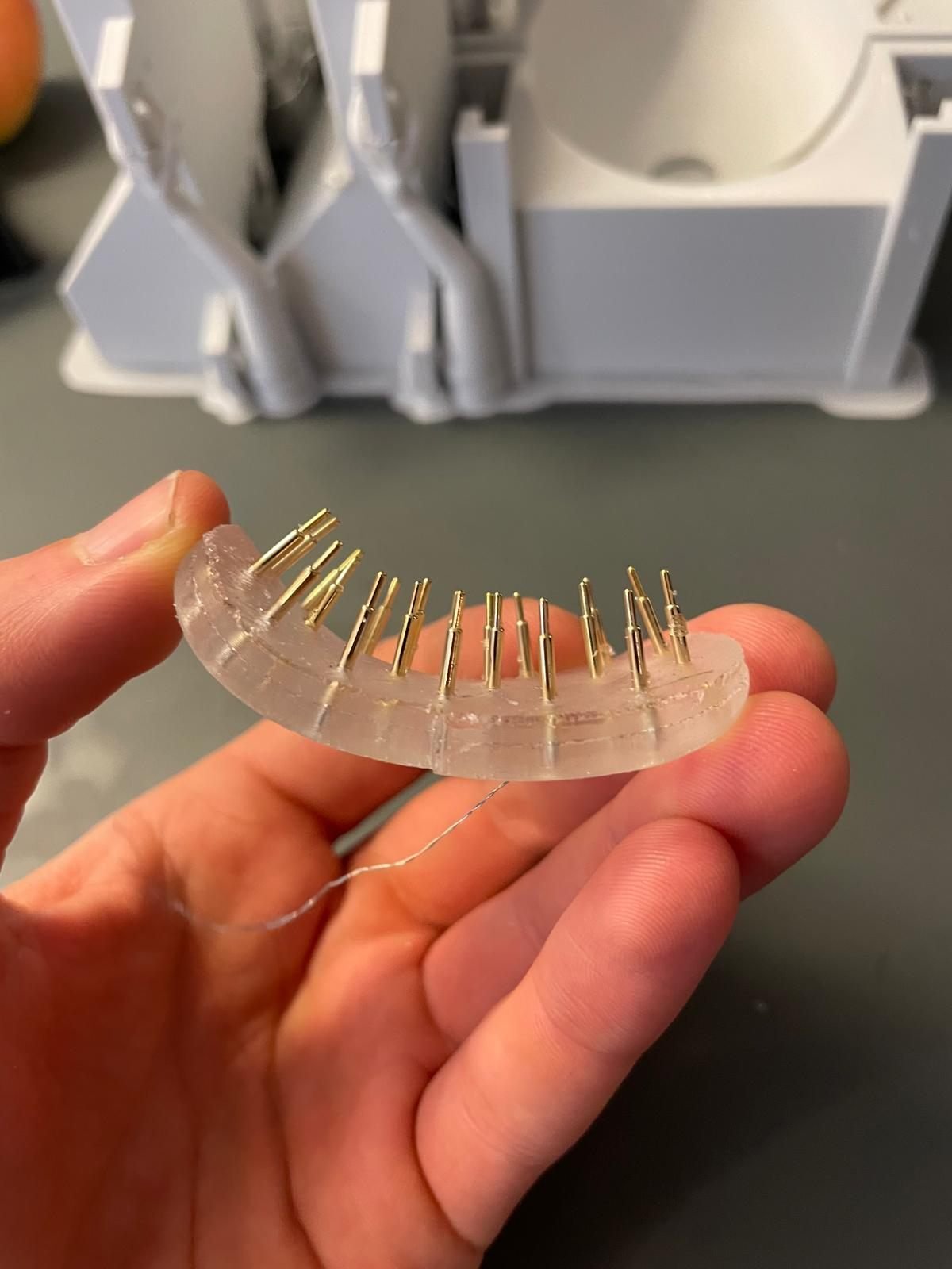 Silicone electrode prototype with gold pins, held in front of its 3D printed mould
